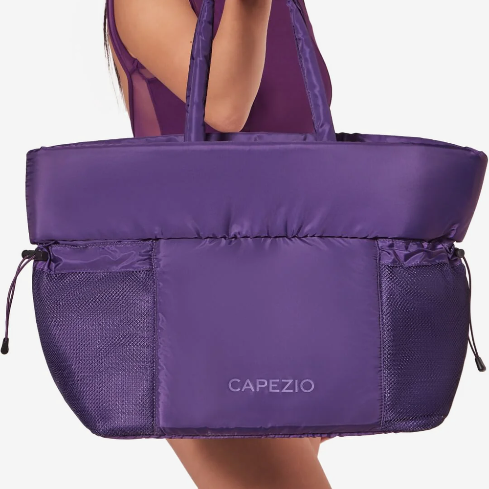Purple tote bag with 'Capezio' branding held by a person on a white background