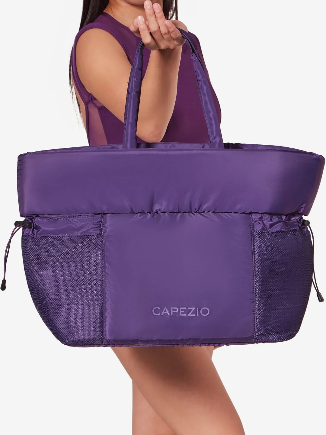 Purple tote bag with 'Capezio' branding held by a person on a white background