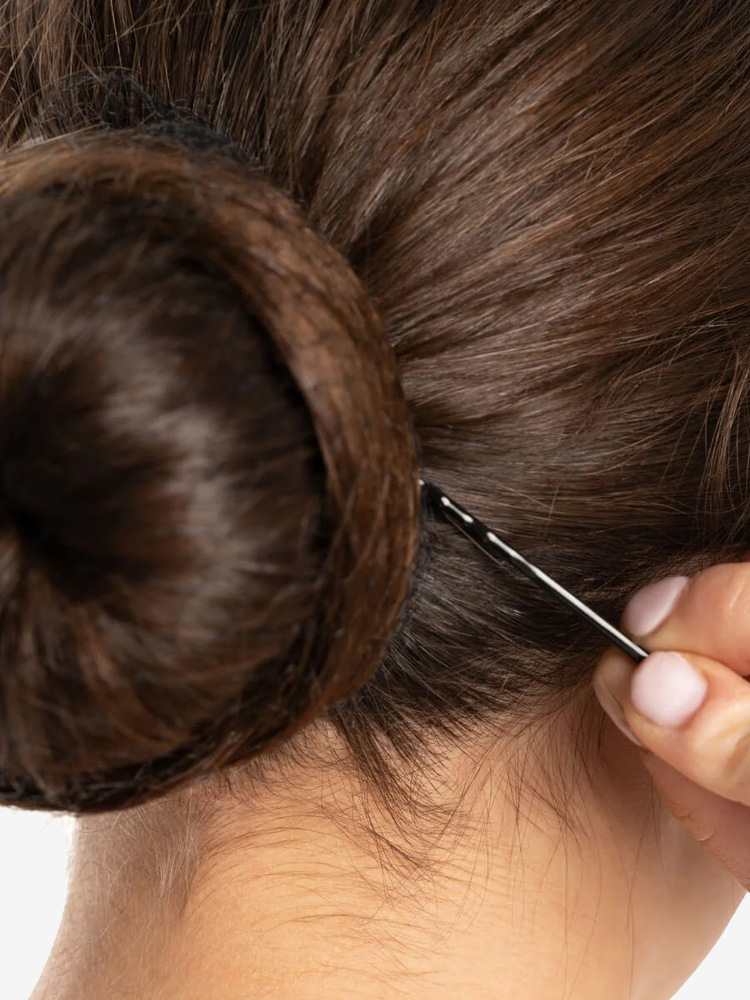 
                      
                        A super close-up of a brunette bun as a bobby pin is being placed into the bun to help secure it.
                      
                    
