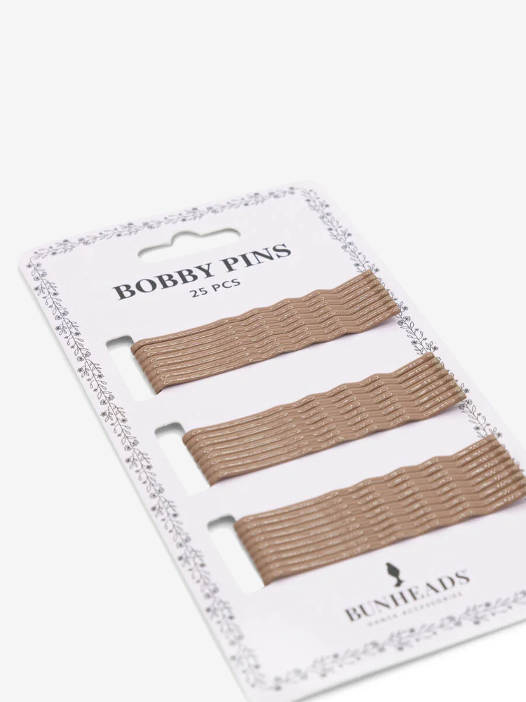 
                      
                        A single sleeve of 25 light brown bobby pins lays at an angle against a plain background.
                      
                    