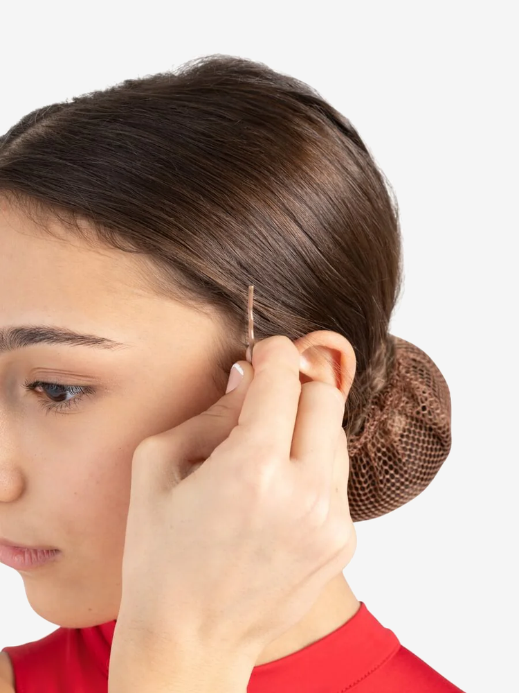 
                      
                        A close-up of a young female with brunette hair in a bun sliding a single bobby pin into the side of her hair. The hint of a red leotard is showing.
                      
                    