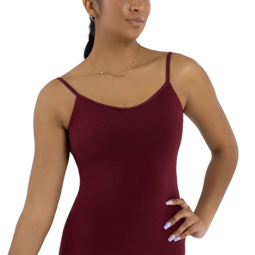 
                      
                        A female dancer with pulled back hair and long styled nails stands with one hand on hip, wearing a light gold necklace and burgundy, spaghetti strap leotard.
                      
                    