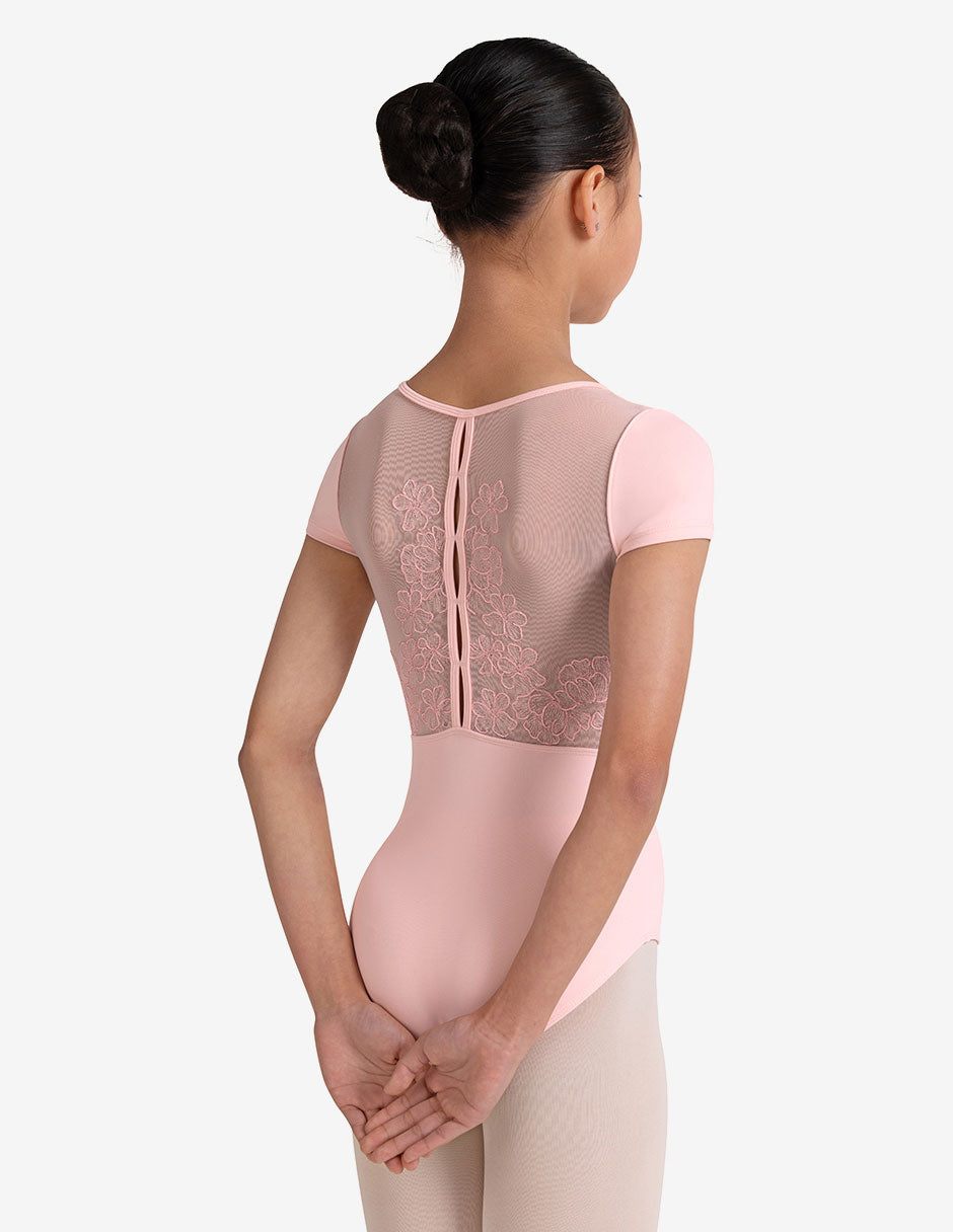 Young girl with black bun wearing a pink ballet leotard with mesh back on a white background