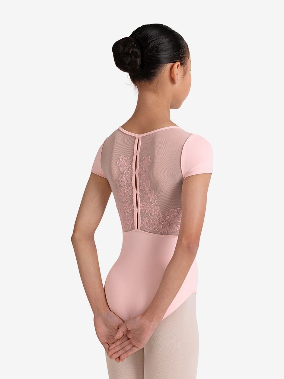 Young girl with black bun wearing a pink ballet leotard with mesh back on a white background