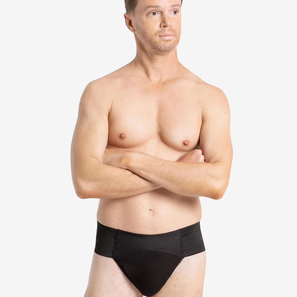 A man with short brown hair is standing against a plain background. He is shirtless and wearing a black-colored compression garment. He has a neutral expression and is looking slightly off to the side.