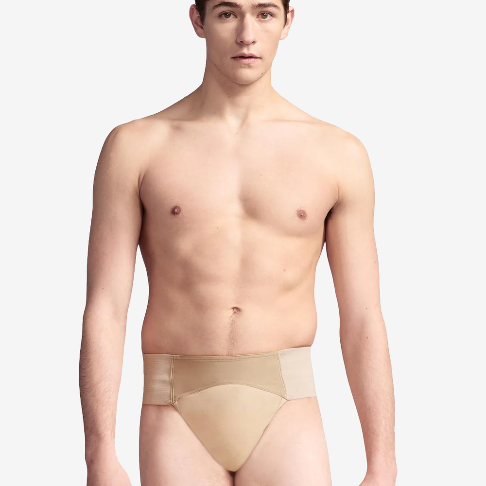 A young man with short brown hair is standing against a plain light grey background. He is shirtless and wearing a beige-colored compression garment. He has a neutral expression and is looking directly at the camera.