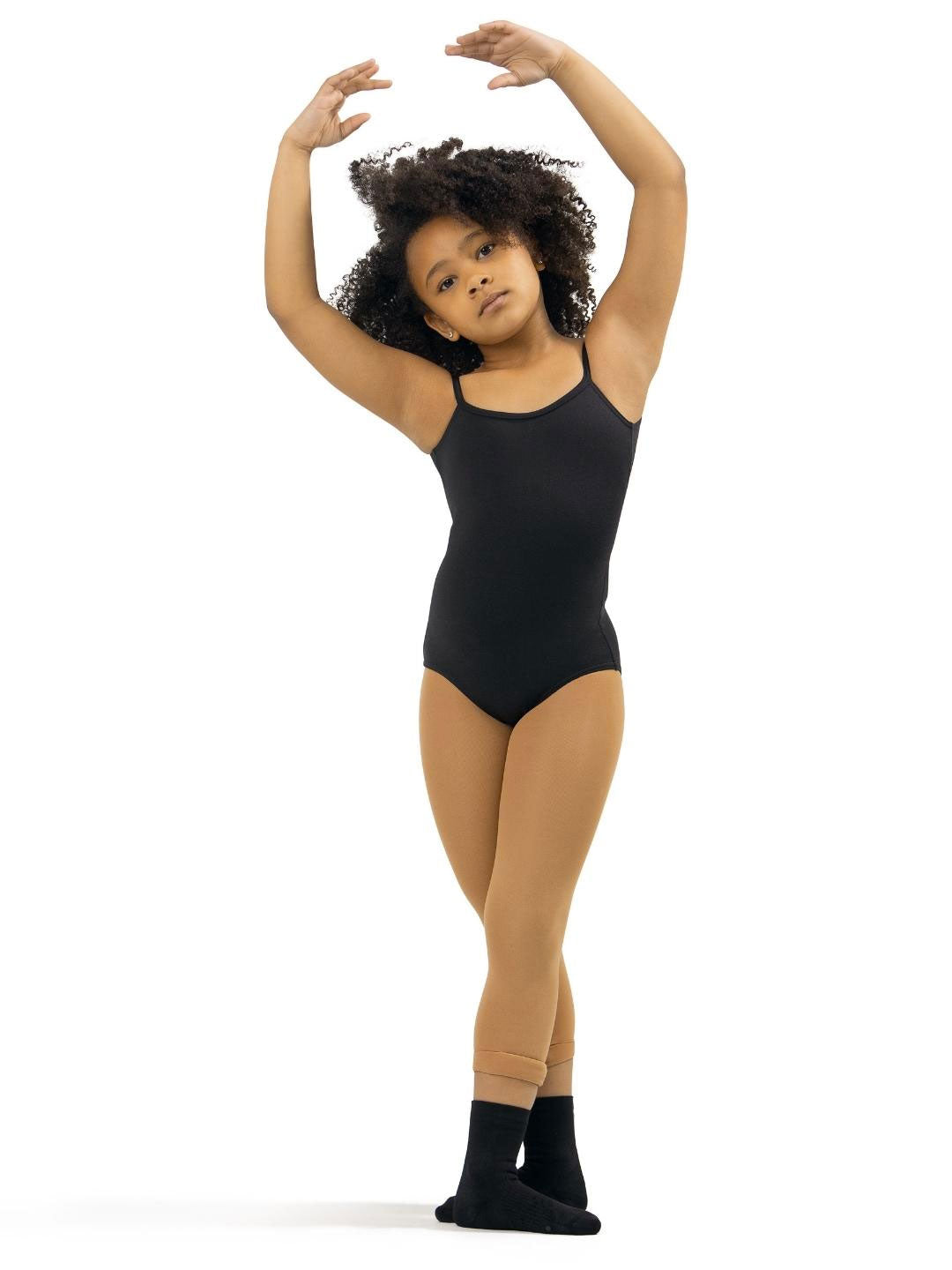 A young girl in a ballet pose. She is wearing a black leotard, light brown skintone tights, and black dance socks. Her arms are raised above her head, and she stands in fifth position. She has curly hair and a focused expression.