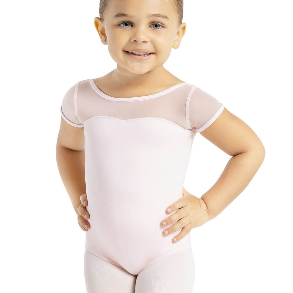 A small child with her hair pulled back, stands with hands on hips, wearing a light pink, short mesh sleeved leotard and ballet pink tights.