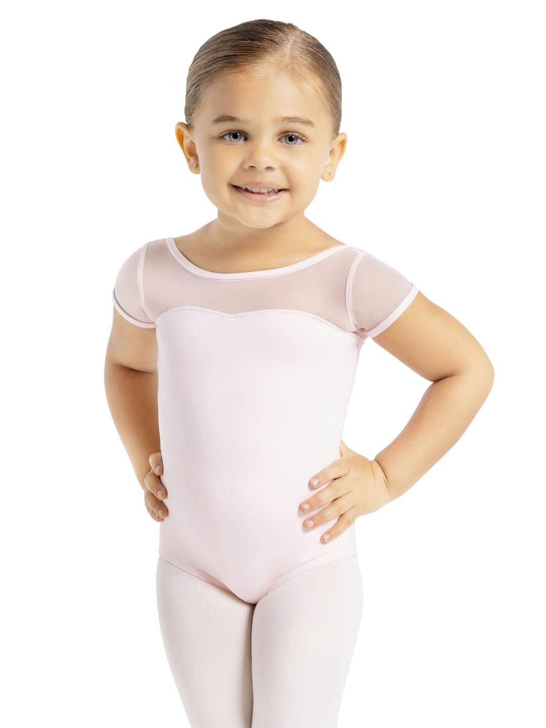 A small child with her hair pulled back, stands with hands on hips, wearing a light pink, short mesh sleeved leotard and ballet pink tights.