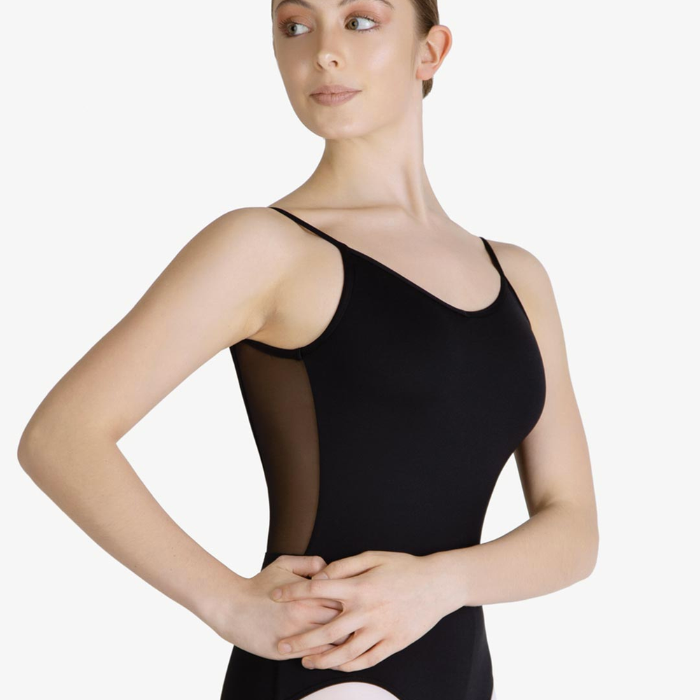 A female wearing a black, spaghetti strap leotard with mesh back, standing with her hands on her hips, hair in a tightly neat bun.