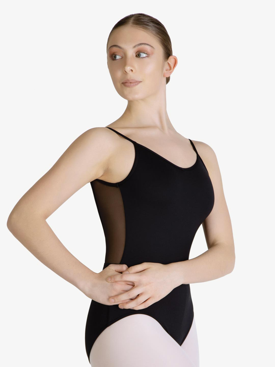 A female wearing a black, spaghetti strap leotard with mesh back, standing with her hands on her hips, hair in a tightly neat bun.