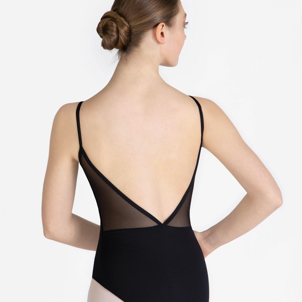 A female standing with her back facing us, hand on hips, wearing a black leotard with a mesh v-shaped low back, hair in a ballet bun.