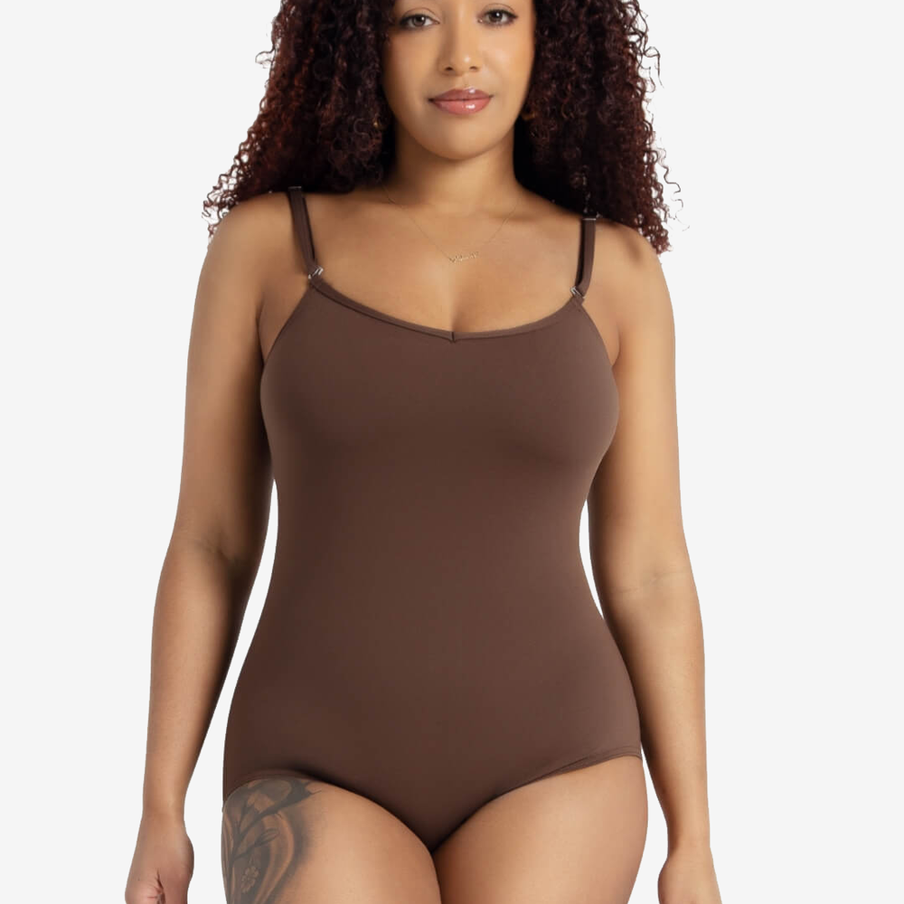 
                      
                        A female dancer with dark curly hair stands against a light grey background. She is wearing an espresso colored, spaghetti strap leotard. She has a tattoo on one leg and pink, pointed nails.
                      
                    