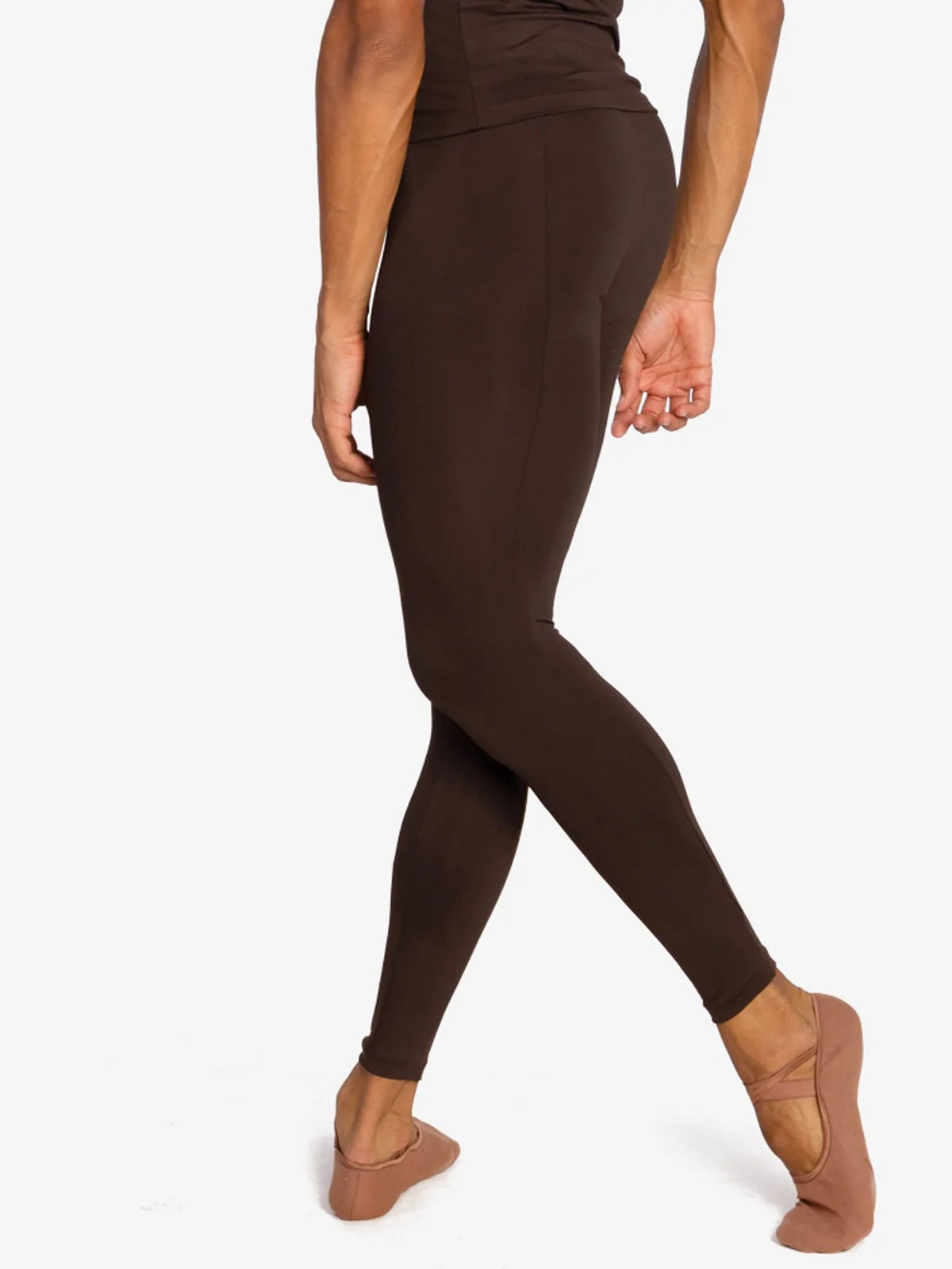 A close-up of the back of a male dancer wearing coffee colored tight leggings. His back leg is extended slightly behind and supported on the toes. 