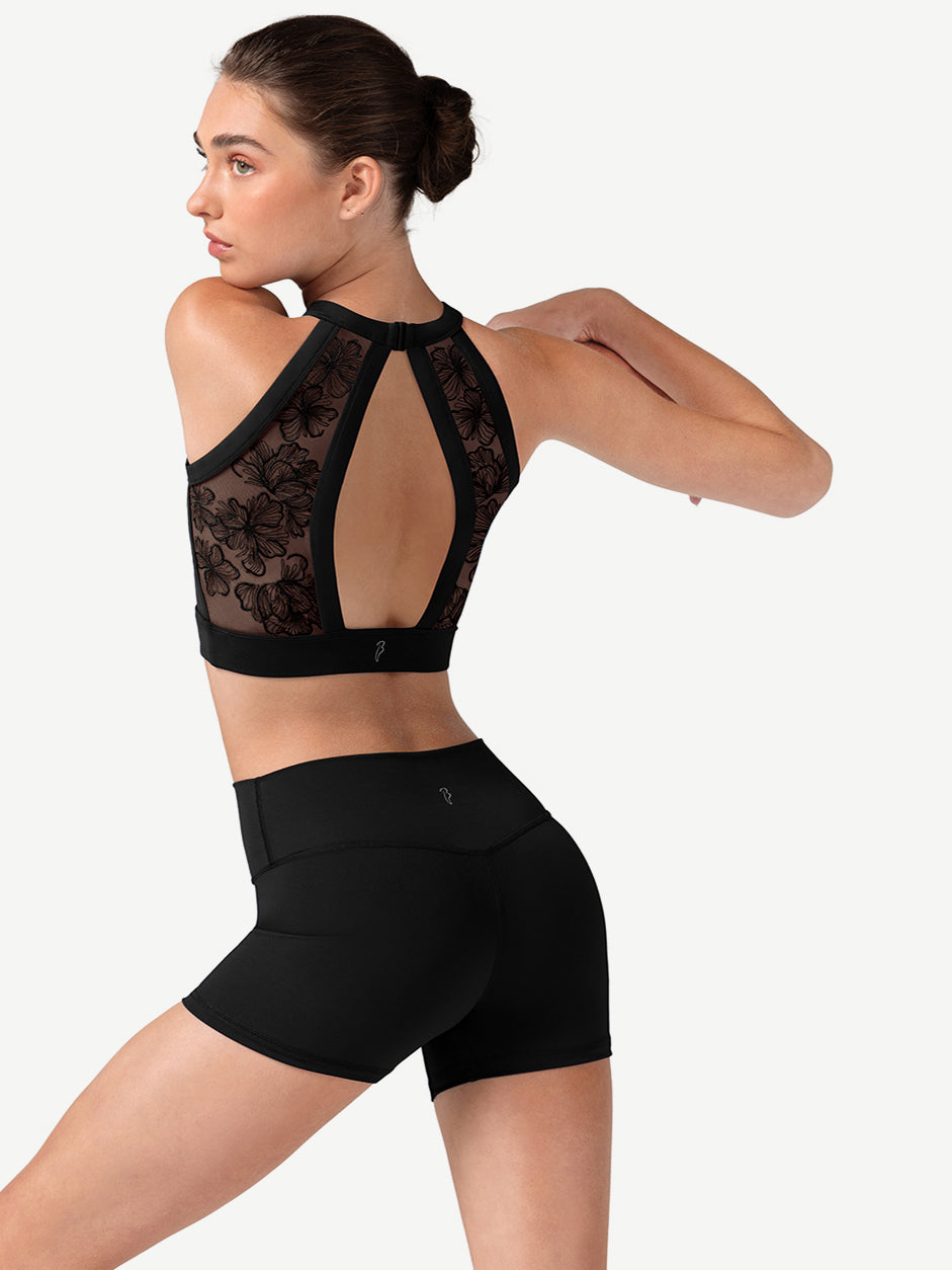 Woman wearing a black lace sports bra and shorts on a white background