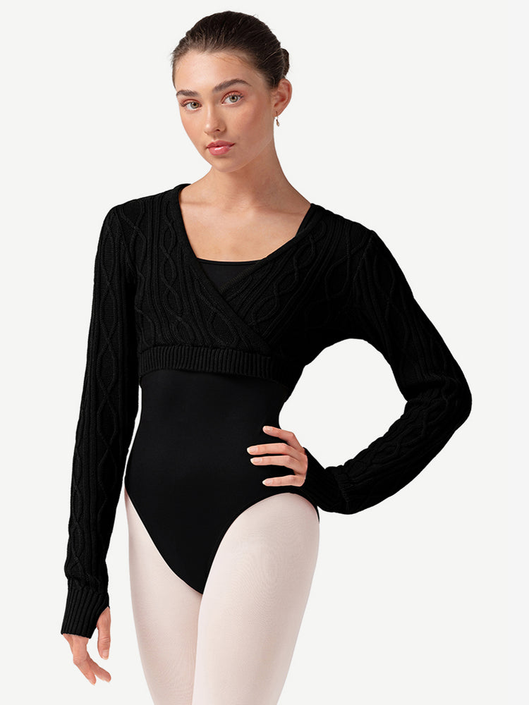 Woman wearing a black long-sleeve sweater over a leotard and ballet pink tights on a plain background