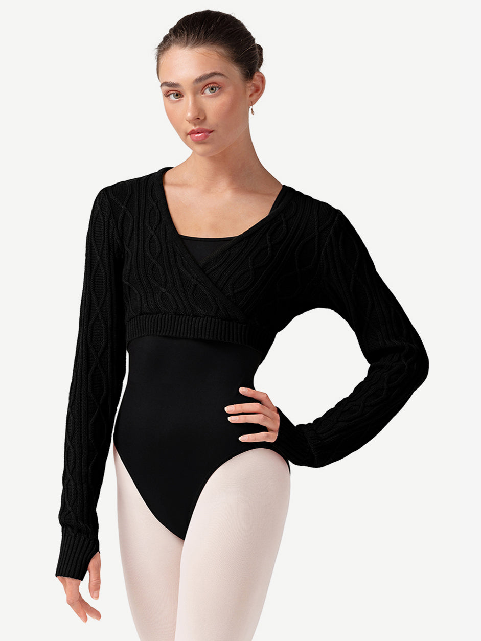 Woman wearing a black long-sleeve sweater over a leotard and ballet pink tights on a plain background