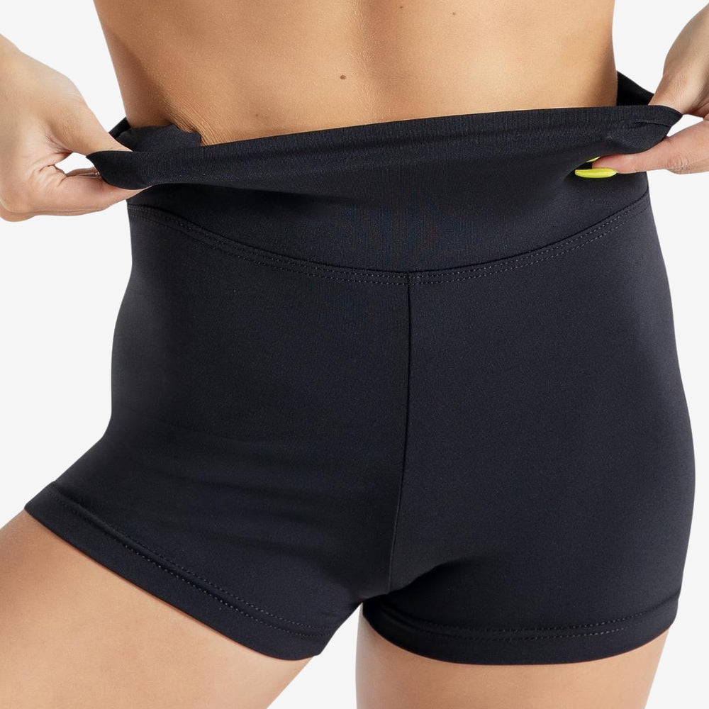 
                      
                        A close-up of a person wearing a blue sports top and black high-waisted athletic shorts. She is adjusting the waistband of the shorts, pulling it up slightly with both hands. The background is plain light grey.
                      
                    