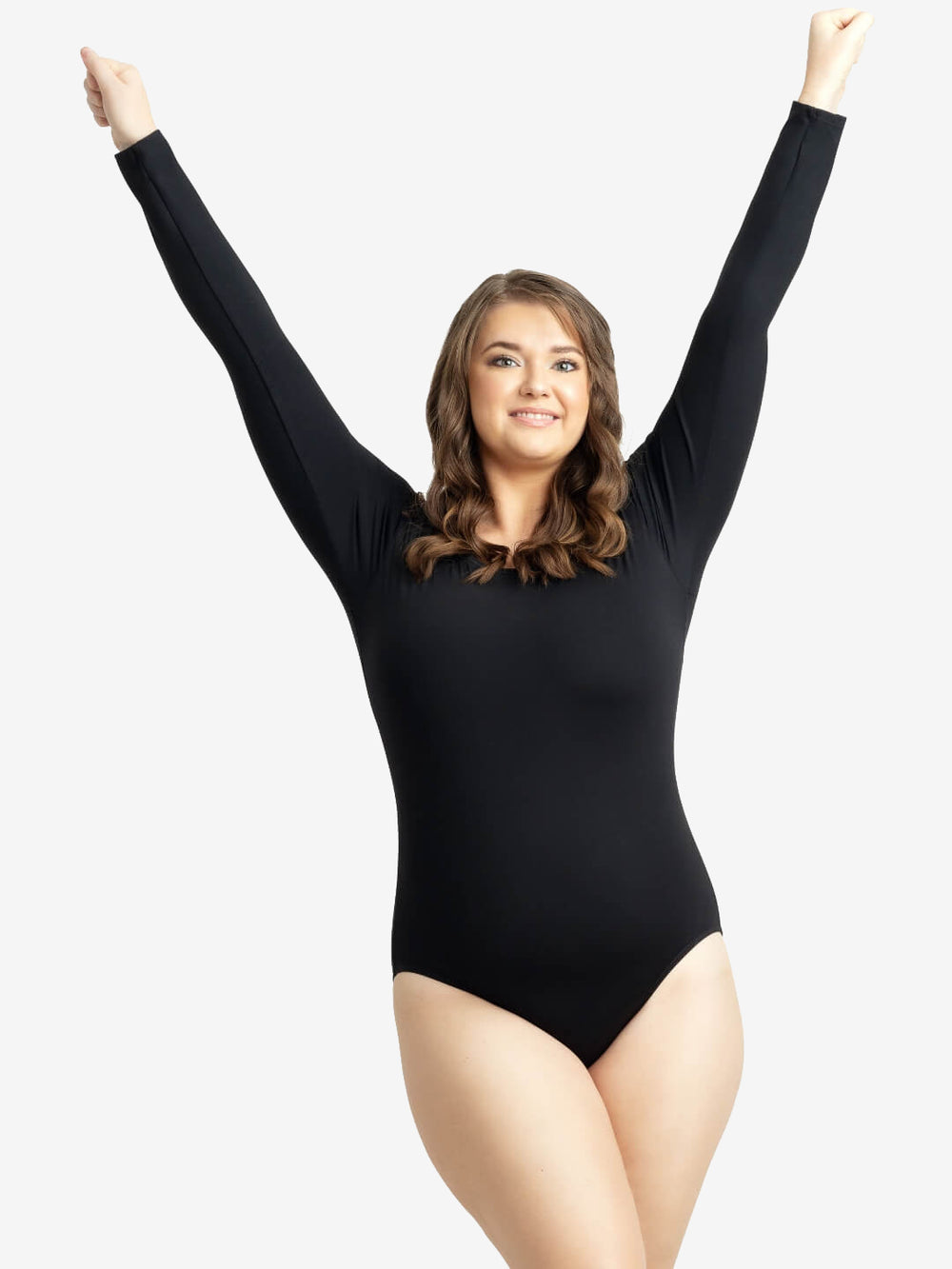 A woman with wavy brown hair is smiling and stretching her arms upwards. She is wearing a long-sleeved black bodysuit and posing confidently against a plain white background.