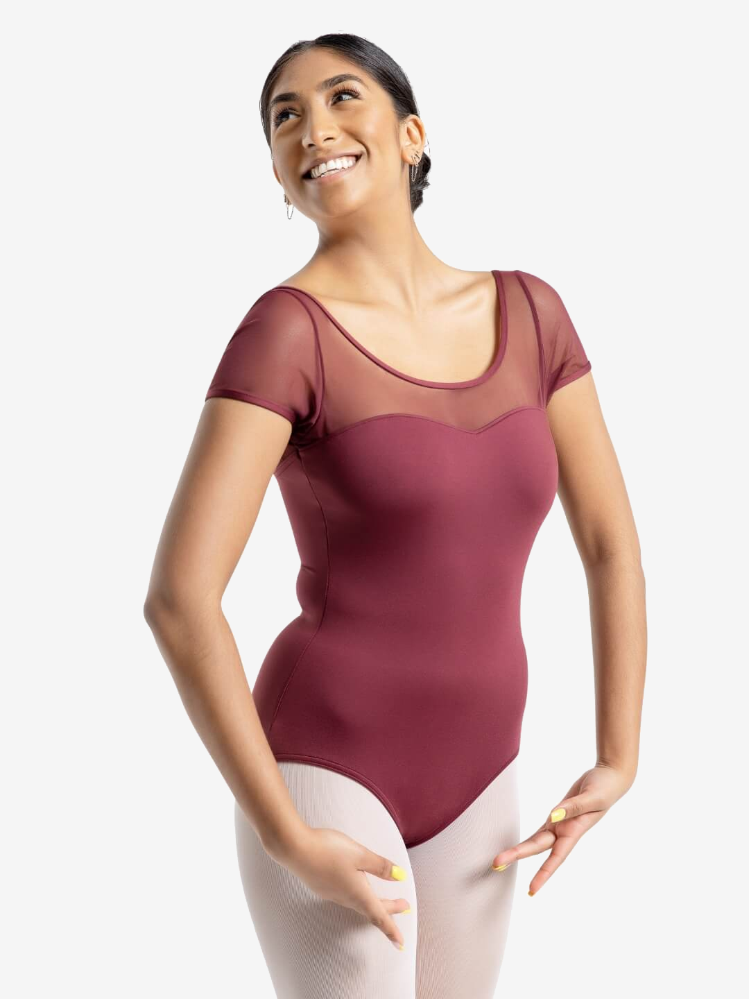 A dancer smiles and looks up and to the side, ballet arms poised in front of her, wearing a burgundy mesh sleeve leotard.