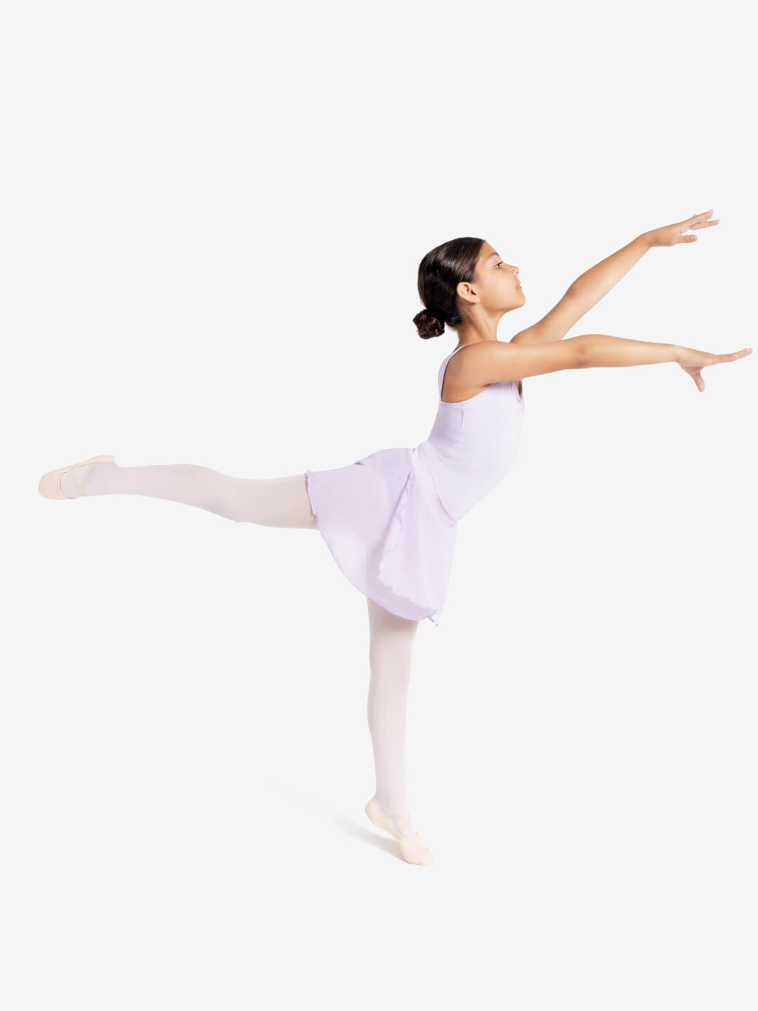 A young ballerina stands in an arabesque pose in a minimalistic setting. She wears a light purple leotard with an attached skirt, white tights, and pink ballet shoes. Her hair is pulled back into a neat bun, and her arms are gracefully extended.