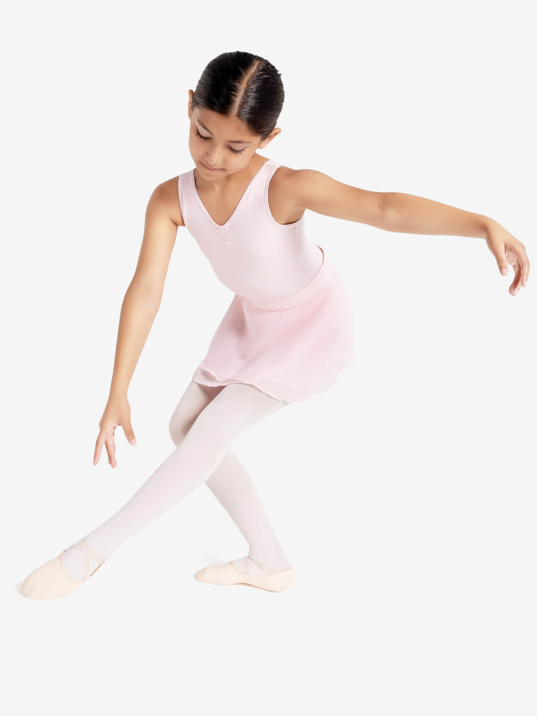 A young child extends her front leg forward and her arm to the side in a graceful ballet pose. She wears a tank style pink leotard, skirt, tights, and ballet shoes.