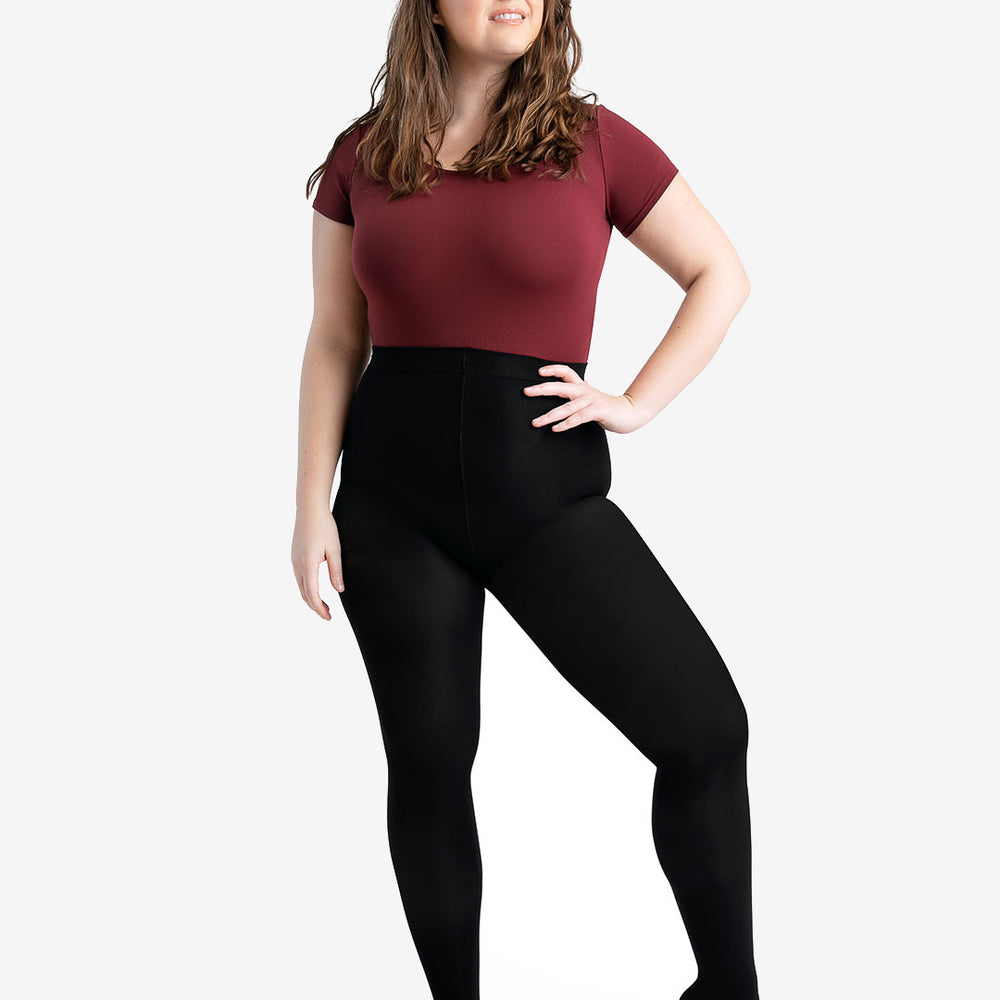 
                      
                        A woman stands with her hand on her hip, she has wavy hair and looks up and to the side. She is wearing a burgundy, short sleeve leotard and black tights on top.
                      
                    