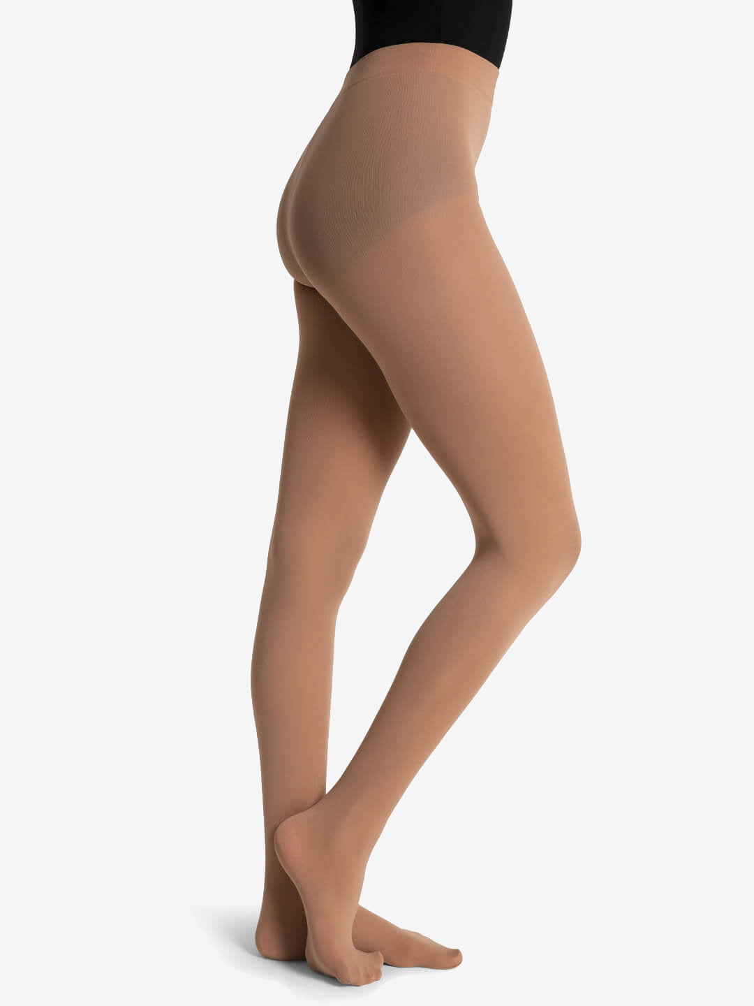 A woman is seen from the waist down wearing light suntan tights over a black leotard, her front foot perched on its toes, against a solid light grey background.