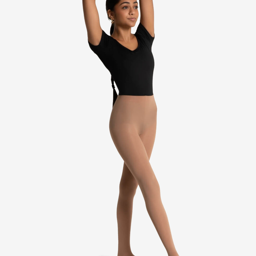 
                      
                        A young woman stands with her weight on her back leg and front leg extended and pointed forward. Her hand are over her head. She is wearing a black short sleeve leotard and tan tights, her long black hair is seen tied behind and flowing down her back. Plain background.
                      
                    
