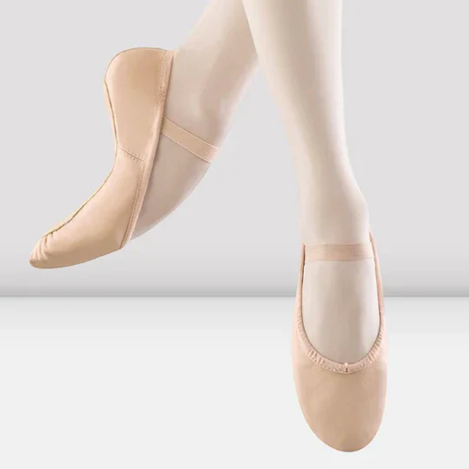 Pink leather ballet shoes worn on a grey background
