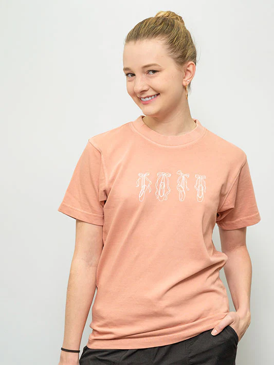 
                      
                        Girl wearing a peach t-shirt with graphic on a plain background
                      
                    