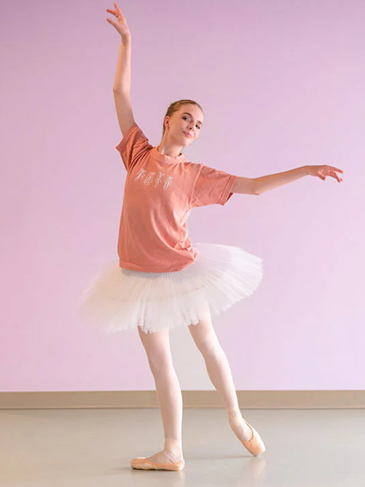Girl wearing a pink t-shirt and white tutu against a light pink wall