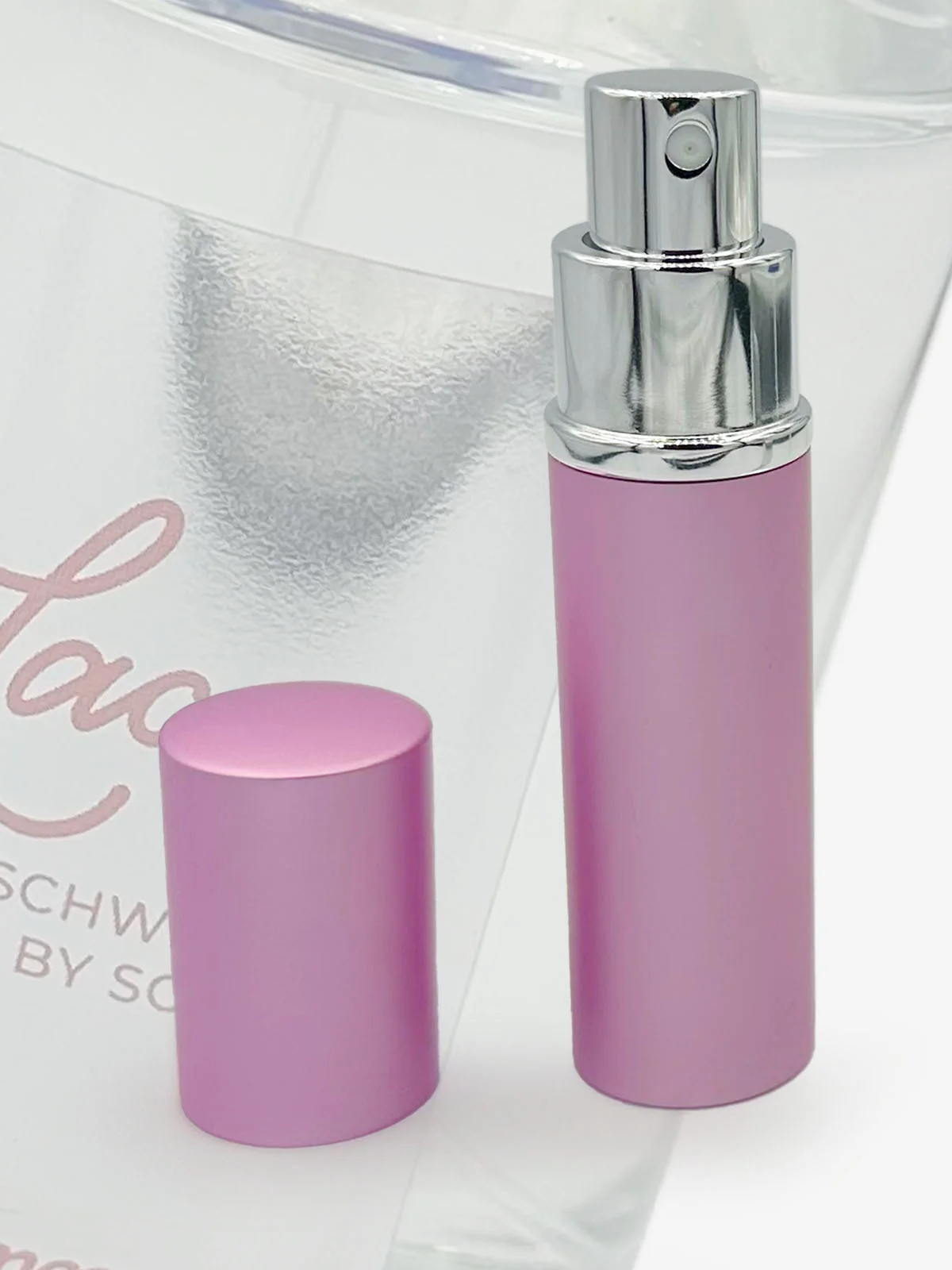 A close-up of a pink perfume bottle, top off to show spray nozzle.