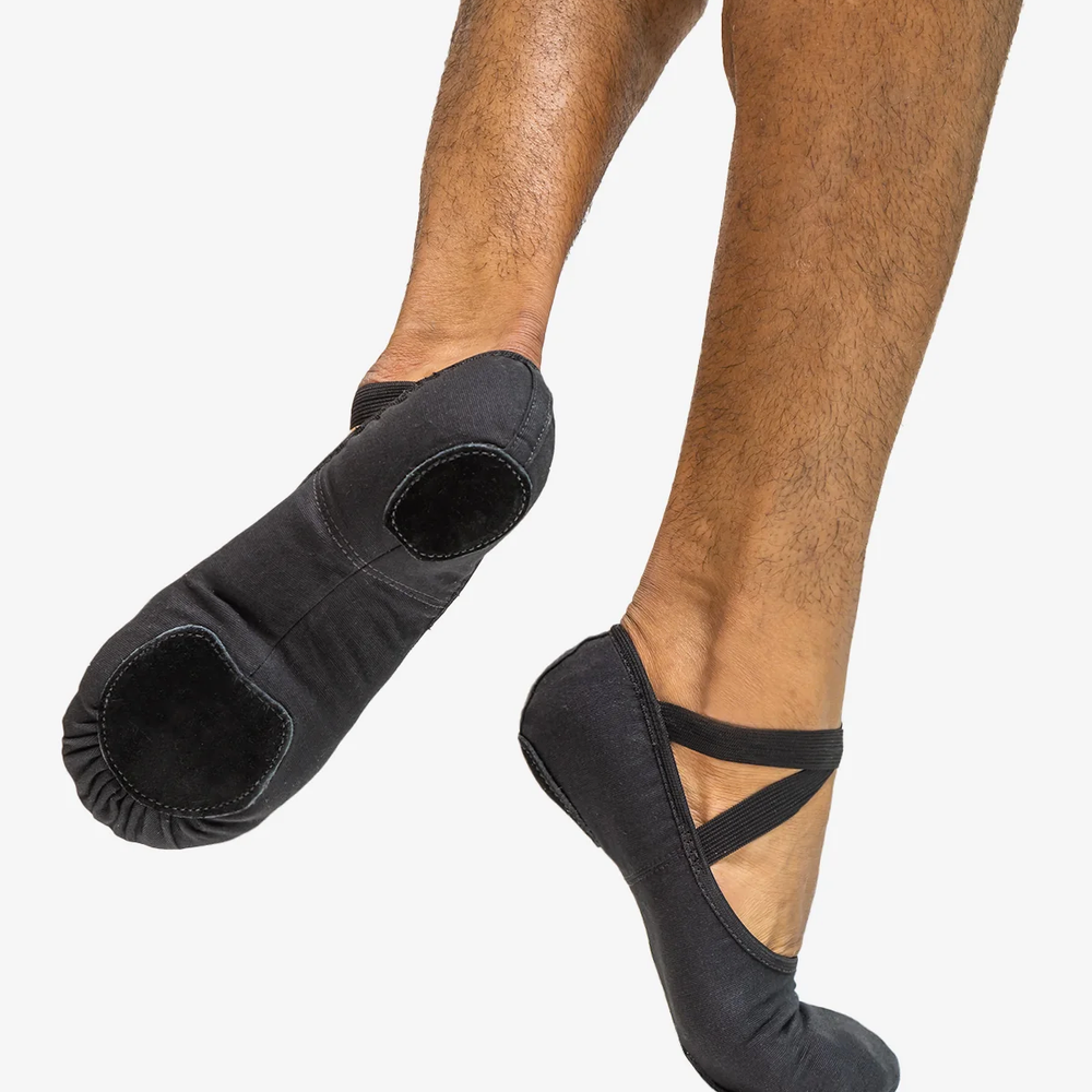 Close-up of a man's legs right foot on releve, back foot lifted showing the bottom of the black ballet shoe