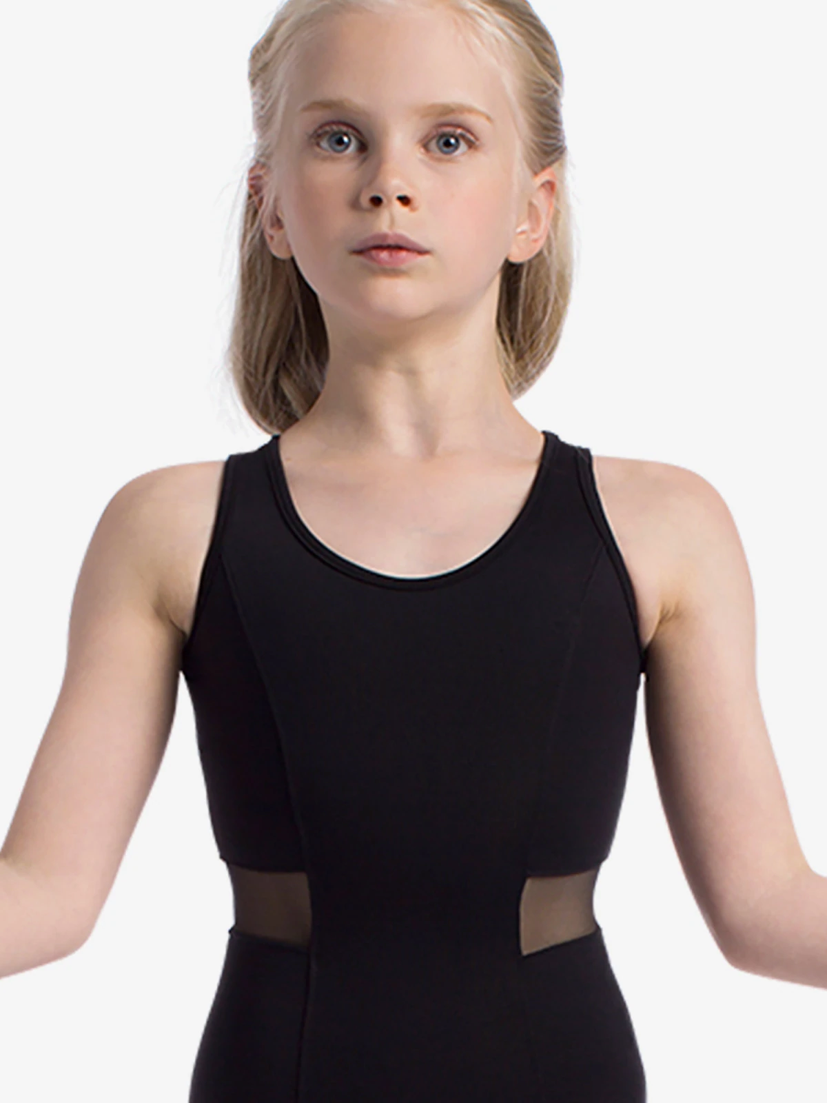 A young blonde girl with her hands held outwards at her sides is wearing a black tank leotard with mesh inserts at the waist.