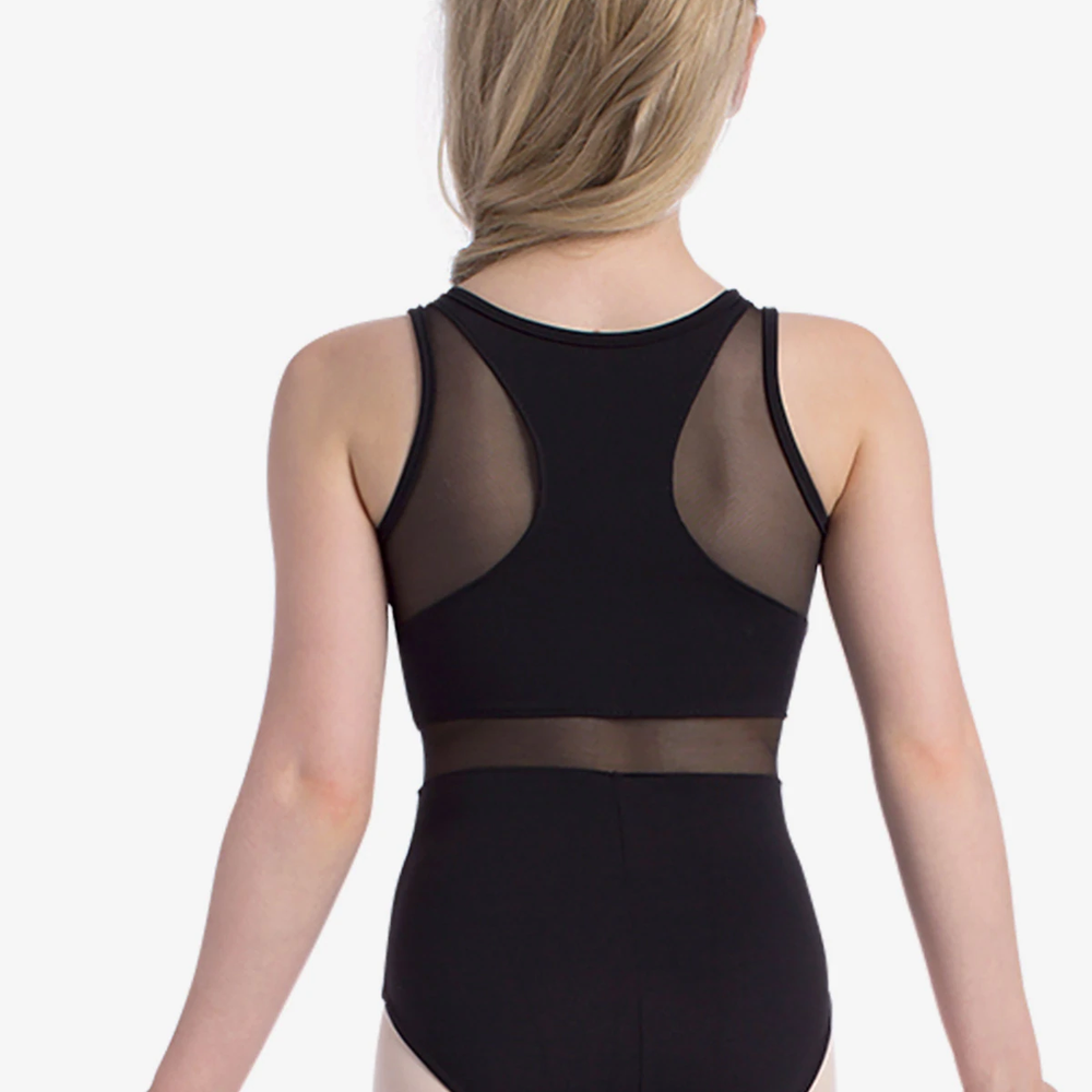A young girl stands with her back to the camera, wearing a black tank leotard with mesh panels on the back and waist. She has long blonde hair styled in a half-up, half-down look and is positioned against a white background.