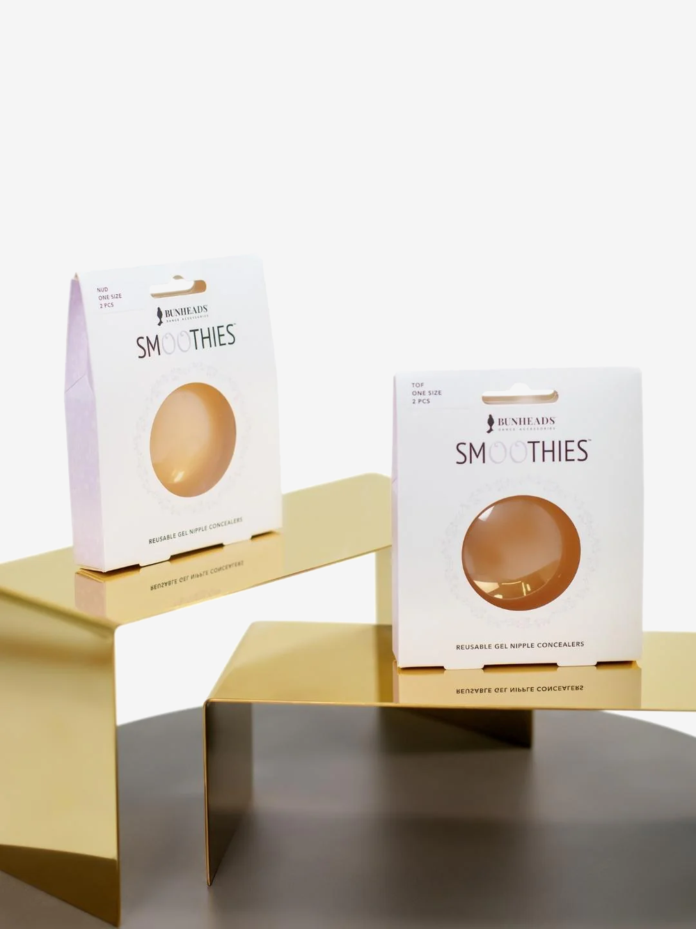 Two boxes of smoothies sit on separate gold stands, staggered, one higher than the other. The back box contains a nude set of smoothies, the front box a toffee set.