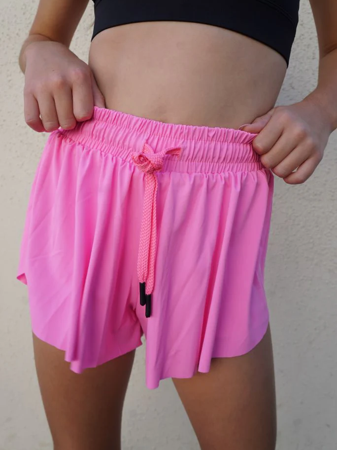 Young girl wearing bright pink shorts with a drawstring on a plain background