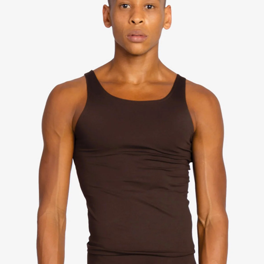 A young man with short dark hair looks at the camera wearing a form fitting skintone coffee colored tank top and leggings.