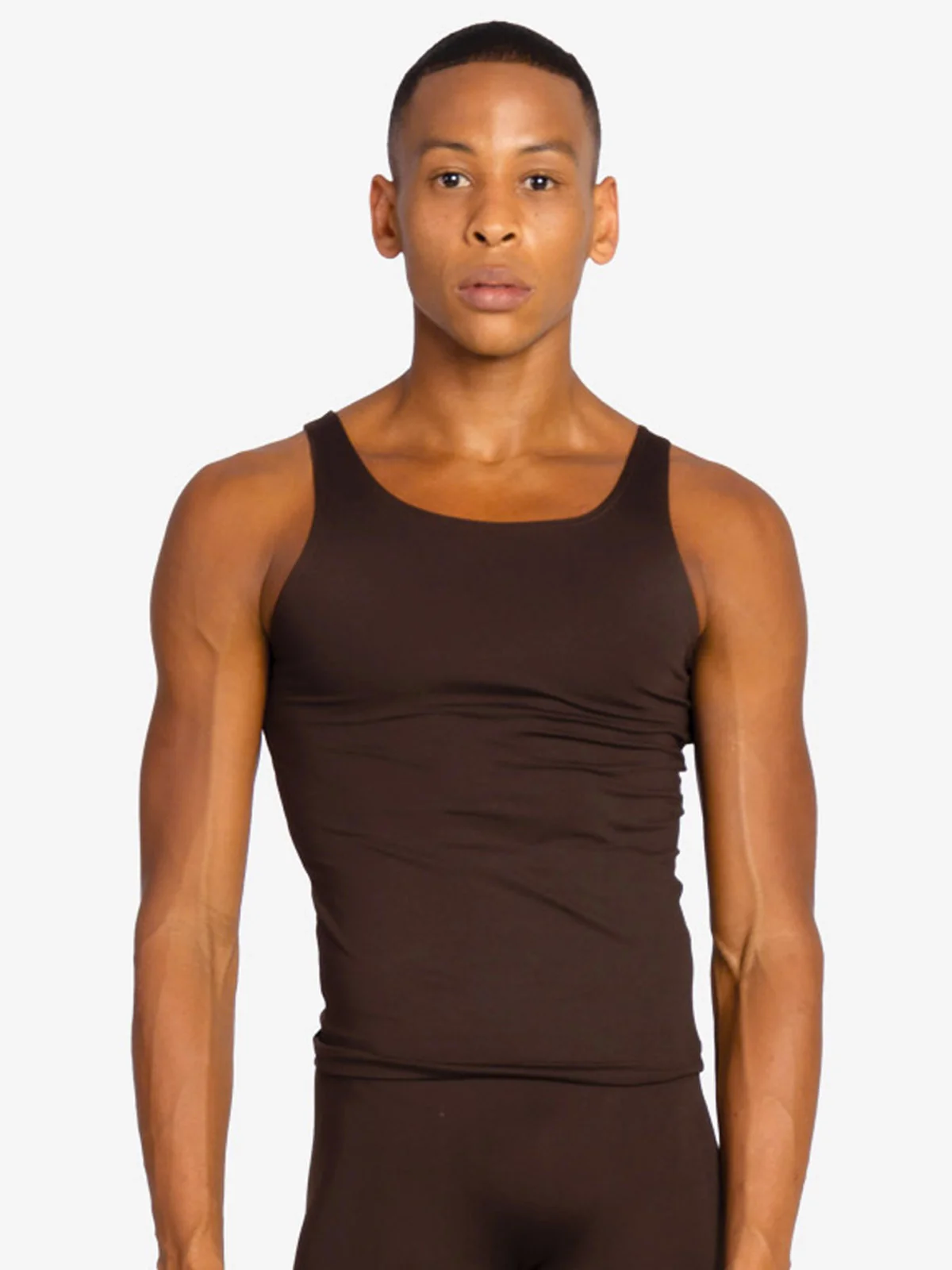 A young man with short dark hair looks at the camera wearing a form fitting skintone coffee colored tank top and leggings.